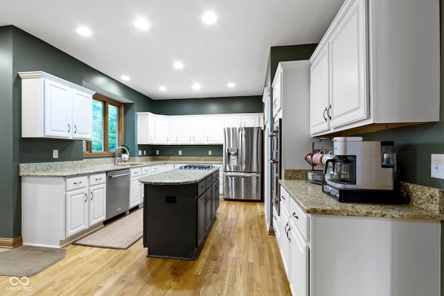 12214 Ridgeside Rd, Indianapolis, IN 46256 - kitchen featuring stainless steel appliances, white cabinets, light wood finished floors, a kitchen island, and light stone countertops