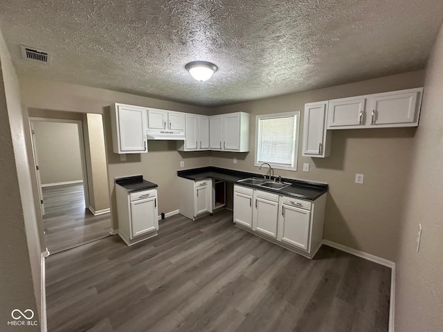 115 Hugo St, Indianapolis, IN 46229 - kitchen with under cabinet range hood, dark wood-style floors, white cabinetry, a textured ceiling, and dark countertops