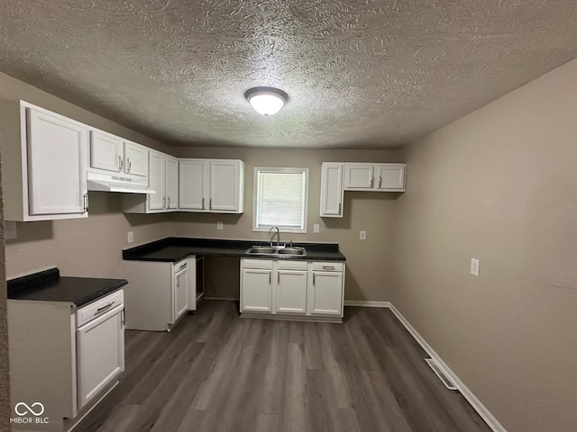 115 Hugo St, Indianapolis, IN 46229 - kitchen featuring a textured ceiling, dark wood-style flooring, white cabinetry, under cabinet range hood, and dark countertops