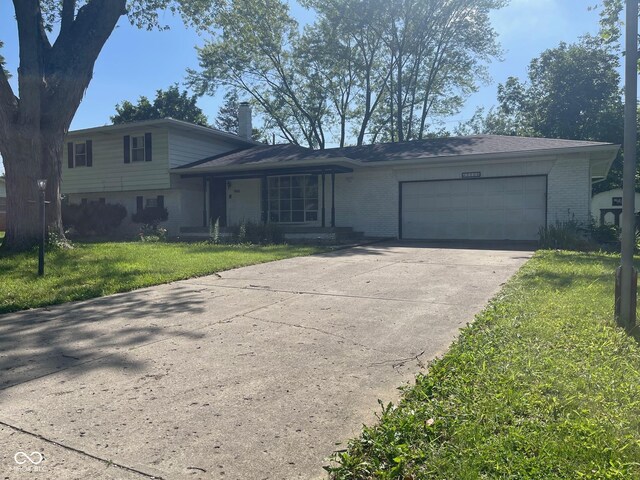 8008 Cherington Dr, Indianapolis, IN 46227 - split level home featuring an attached garage, brick siding, a front yard, and concrete driveway