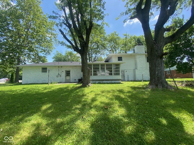 8008 Cherington Dr, Indianapolis, IN 46227 - back of property with a sunroom, a lawn, a chimney, and brick siding
