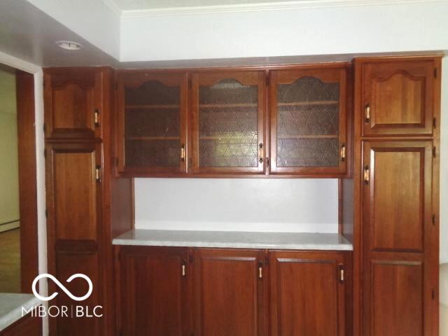 3253 W 34th St, Indianapolis, IN 46222 - kitchen featuring light countertops, glass insert cabinets, brown cabinetry, and ornamental molding