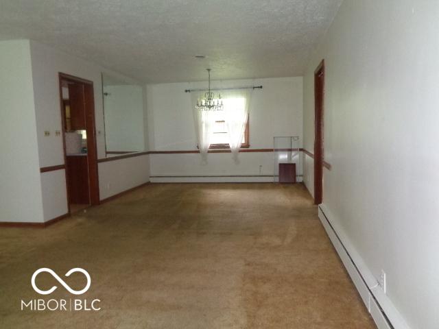 3253 W 34th St, Indianapolis, IN 46222 - unfurnished dining area featuring baseboard heating, a baseboard radiator, a chandelier, light colored carpet, and a textured ceiling
