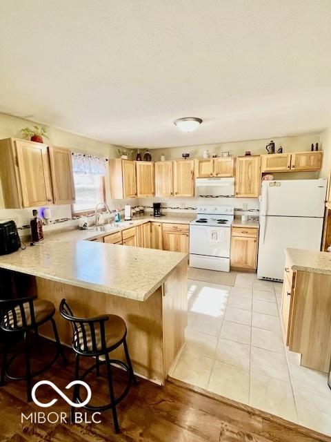 409 N Kyle St, Edinburgh, IN 46124 - kitchen featuring white appliances, light brown cabinets, a peninsula, under cabinet range hood, and light countertops