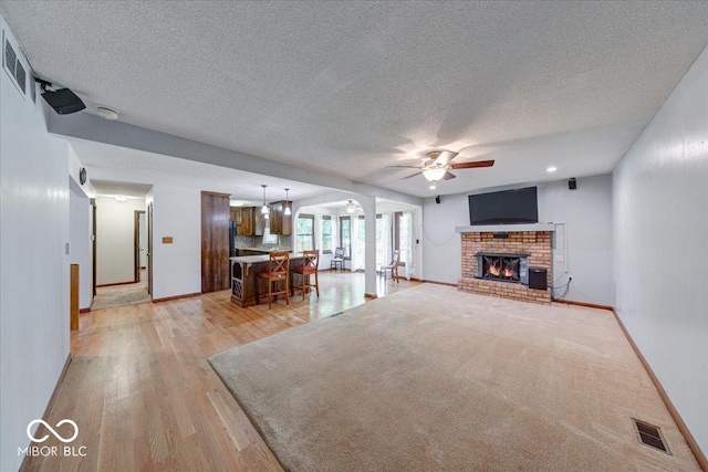 11 N Restin Rd, Greenwood, IN 46142 - living room with ceiling fan, a textured ceiling, light wood-style flooring, and a brick fireplace