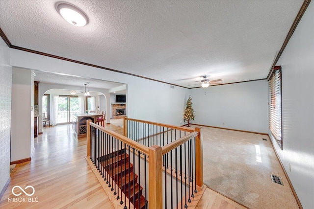 11 N Restin Rd, Greenwood, IN 46142 - hallway featuring arched walkways, a textured ceiling, ornamental molding, an upstairs landing, and light wood-type flooring