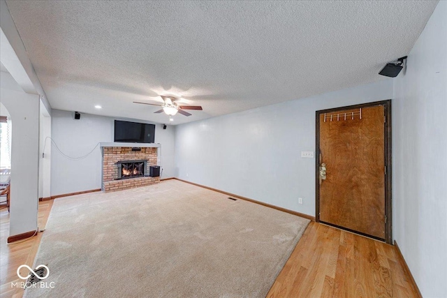 11 N Restin Rd, Greenwood, IN 46142 - unfurnished living room featuring ceiling fan, a brick fireplace, a textured ceiling, and light wood-style flooring