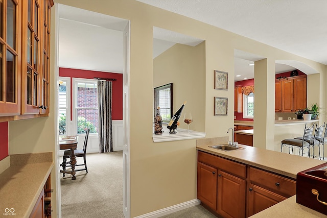 4704 Pearcrest Way, Greenwood, IN 46143 - kitchen featuring light countertops, a wainscoted wall, light colored carpet, brown cabinetry, and arched walkways