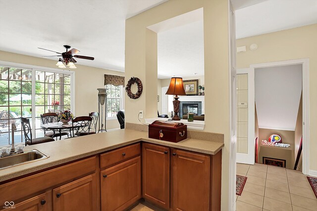 4704 Pearcrest Way, Greenwood, IN 46143 - kitchen with ceiling fan, a glass covered fireplace, light tile patterned floors, brown cabinetry, and light countertops