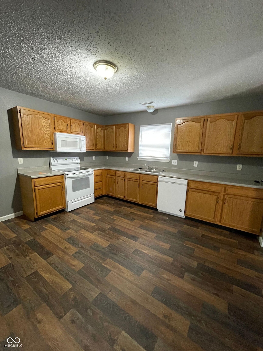 3929 Roundwood Dr, Indianapolis, IN 46235 - kitchen featuring white appliances, light countertops, dark wood-style floors, a textured ceiling, and brown cabinetry