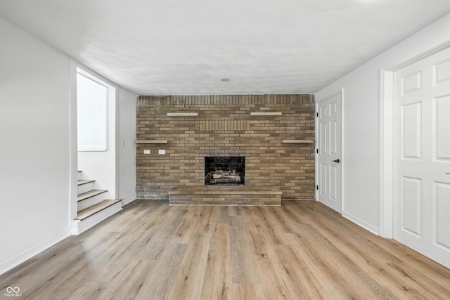 1011 Robin Dr, Anderson, IN 46013 - unfurnished living room featuring light wood-type flooring, a fireplace, stairs, and brick wall