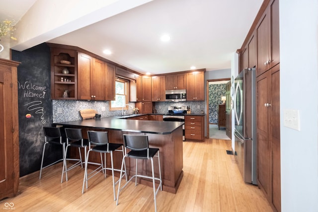 3711 Tara Ct, Carmel, IN 46074 - kitchen featuring a peninsula, stainless steel appliances, dark countertops, light wood-style floors, and tasteful backsplash