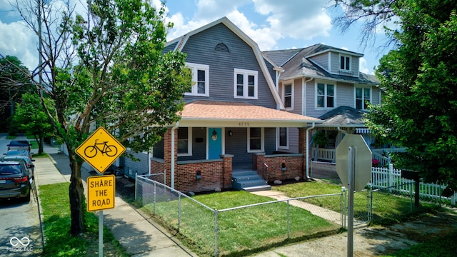 4155 Graceland Ave, Indianapolis, IN 46208 - view of front of house with covered porch, a gambrel roof, brick siding, a fenced front yard, and roof with shingles