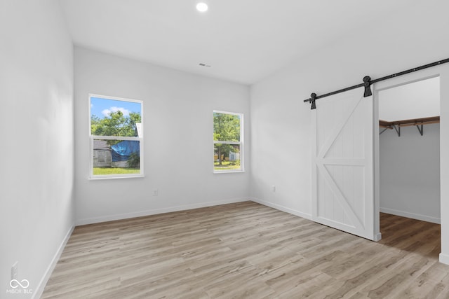 2709 Station St, Indianapolis, IN 46218 - unfurnished bedroom featuring a barn door, light wood-style flooring, a spacious closet, and recessed lighting