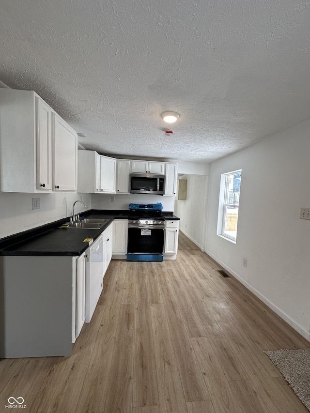 1256 Kappes St, Indianapolis, IN 46221 - kitchen featuring appliances with stainless steel finishes, dark countertops, a textured ceiling, white cabinets, and light wood-type flooring