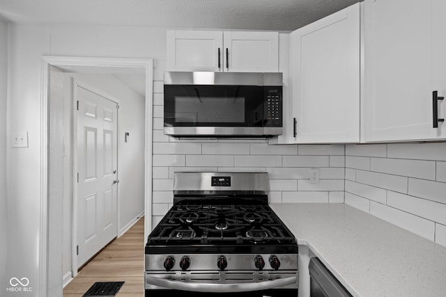 1730 S State Ave, Indianapolis, IN 46203 - kitchen with stainless steel appliances, light wood-type flooring, decorative backsplash, light stone countertops, and white cabinets