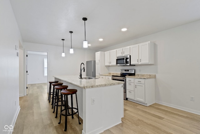 4129 Cornelius Ave, Indianapolis, IN 46208 - kitchen with stainless steel appliances, light wood finished floors, a kitchen bar, a kitchen island with sink, and white cabinets