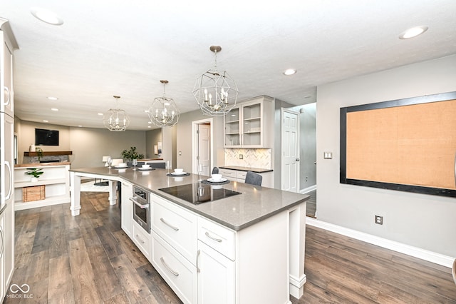 5826 Winding Way Ln, Indianapolis, IN 46220 - kitchen with black electric stovetop, a chandelier, glass insert cabinets, a kitchen island, and dark wood-style floors