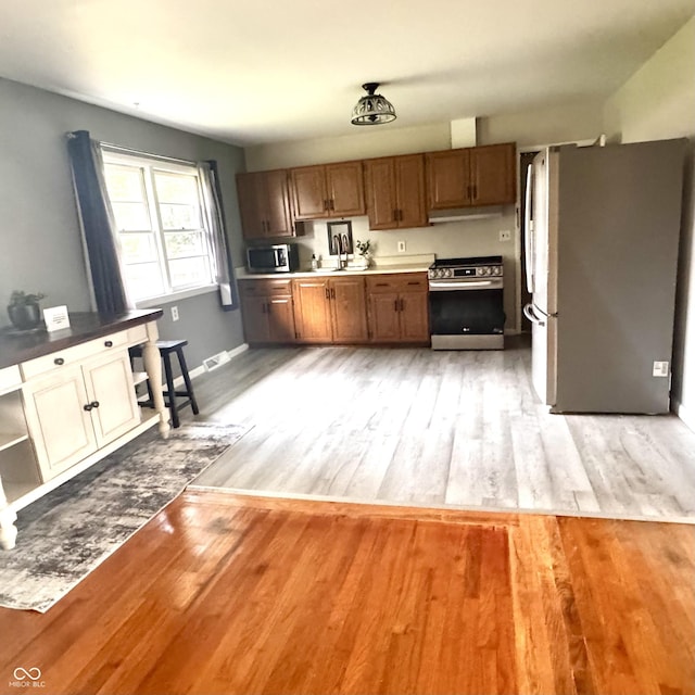336 Brookside Ln, Plainfield, IN 46168 - kitchen featuring stainless steel appliances, light wood-style flooring, under cabinet range hood, and brown cabinetry