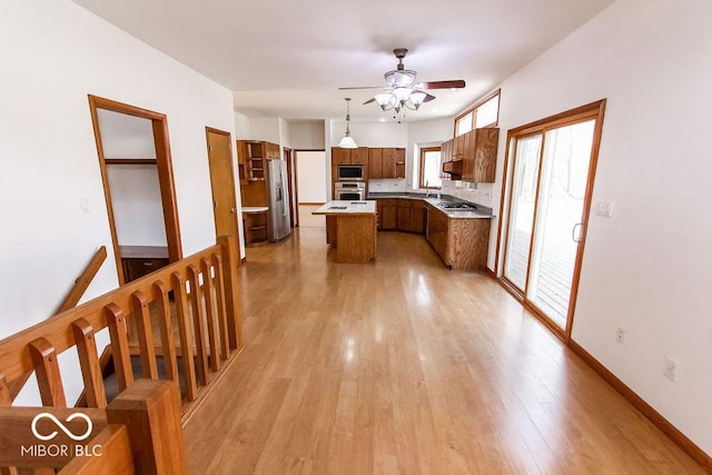 3948 S Woodfield Dr, New Palestine, IN 46163 - kitchen featuring stainless steel appliances, a kitchen island, a ceiling fan, brown cabinetry, and light wood finished floors