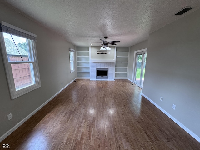1206 Brownswood Dr, Brownsburg, IN 46112 - unfurnished living room with dark wood finished floors, ceiling fan, built in features, a fireplace with flush hearth, and a textured ceiling