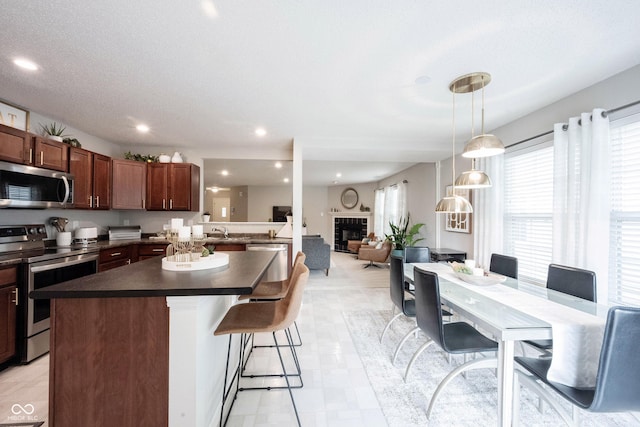 14459 Forsythia Ln, Fishers, IN 46038 - kitchen with stainless steel appliances, dark countertops, a fireplace, a kitchen island, and a kitchen breakfast bar