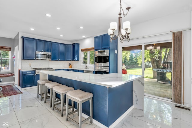 6374 Timberbluff Cir, Avon, IN 46123 - kitchen featuring appliances with stainless steel finishes, blue cabinetry, tasteful backsplash, light marble finish floors, and a chandelier