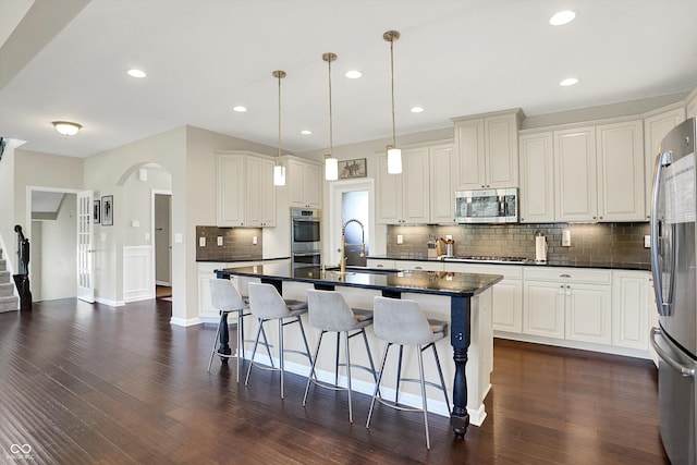16711 Meadow Wood Dr, Noblesville, IN 46062 - kitchen featuring appliances with stainless steel finishes, dark countertops, arched walkways, decorative backsplash, and a kitchen breakfast bar
