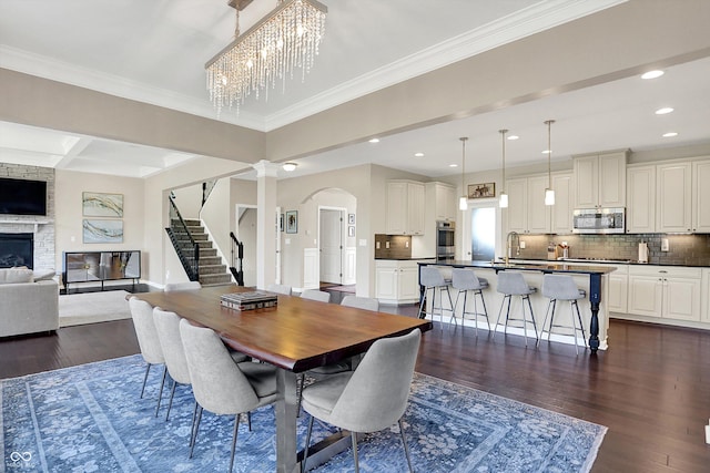 16711 Meadow Wood Dr, Noblesville, IN 46062 - dining space with stairway, dark wood-type flooring, arched walkways, a fireplace, and recessed lighting