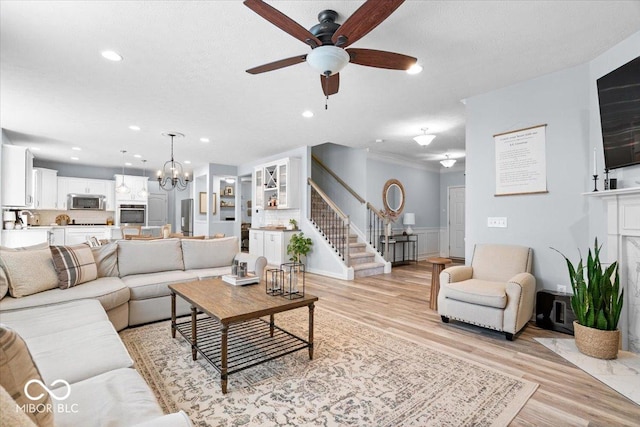 5542 Pennycress Dr, Noblesville, IN 46062 - living room with stairway, a ceiling fan, light wood-style floors, a wainscoted wall, and a chandelier