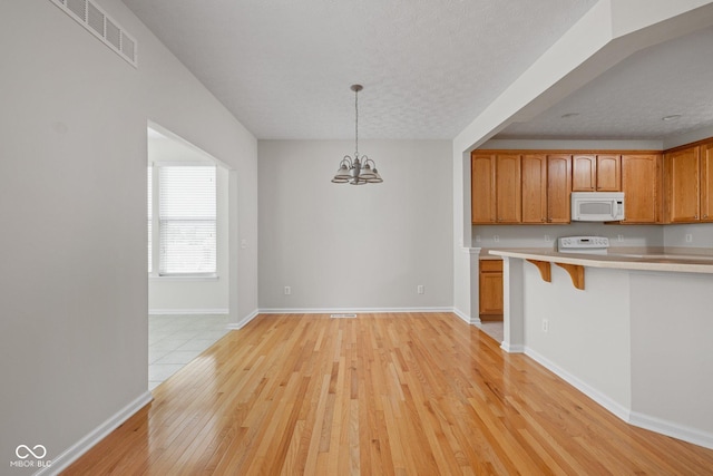 13019 Pinner Ave, Fishers, IN 46037 - kitchen featuring white microwave, light countertops, light wood-style flooring, a chandelier, and a breakfast bar area