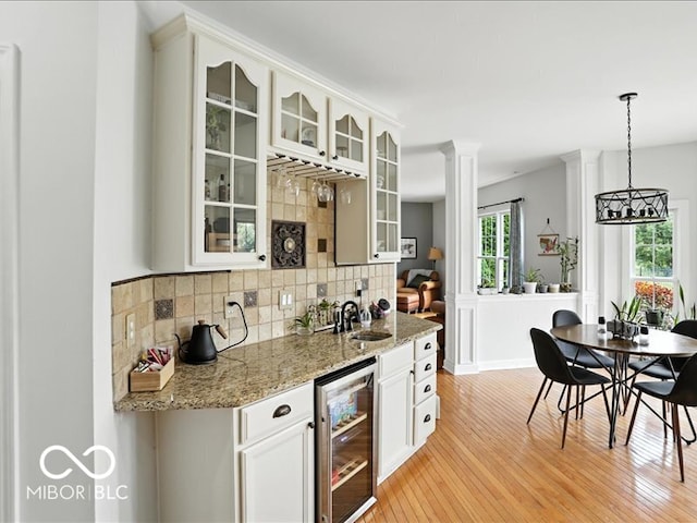 4233 Dartmoor Dr, Greenwood, IN 46143 - indoor wet bar featuring wine cooler, decorative backsplash, light wood finished floors, hanging light fixtures, and decorative columns