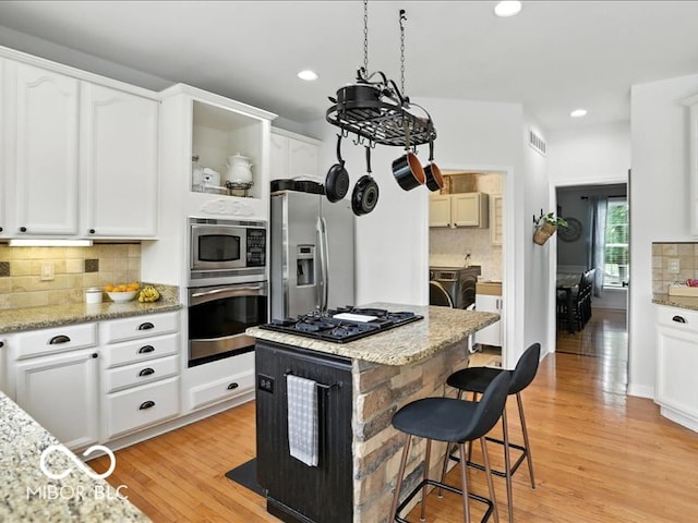 4233 Dartmoor Dr, Greenwood, IN 46143 - kitchen featuring appliances with stainless steel finishes, open shelves, backsplash, washing machine and clothes dryer, and a breakfast bar area