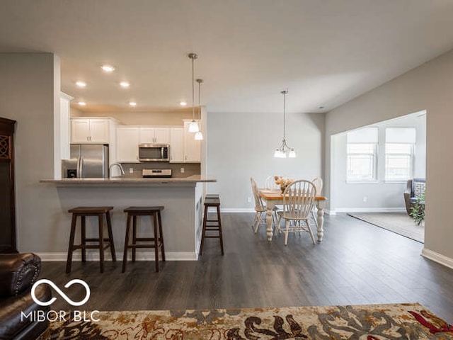 8866 Twain Ln, Indianapolis, IN 46239 - kitchen with appliances with stainless steel finishes, a breakfast bar area, dark wood-type flooring, white cabinetry, and pendant lighting