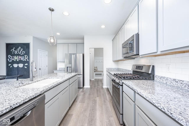 7147 Prelude Rd, Brownsburg, IN 46112 - kitchen featuring appliances with stainless steel finishes, light wood-style flooring, backsplash, light stone counters, and hanging light fixtures