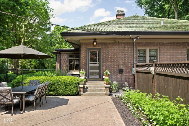 4455 Broadway St, Indianapolis, IN 46205 - back of house with brick siding, a chimney, a tiled roof, outdoor dining space, and a patio