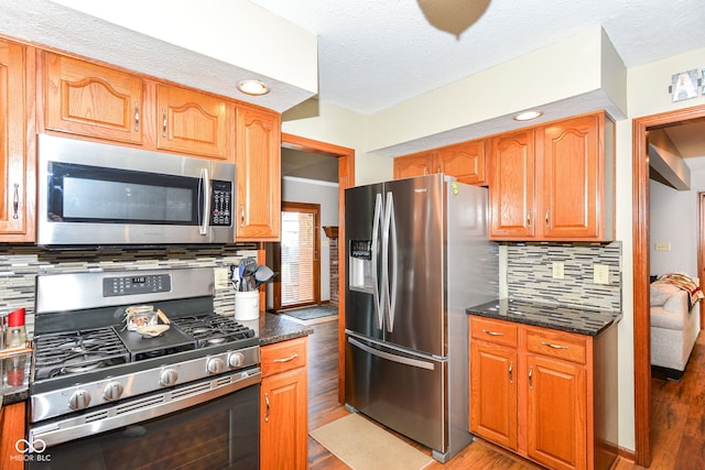 662 Leah Way, Greenwood, IN 46142 - kitchen featuring appliances with stainless steel finishes, light wood-style flooring, tasteful backsplash, dark stone counters, and a textured ceiling
