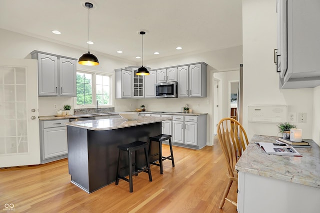 5761 Coopers Hawk Dr, Carmel, IN 46033 - kitchen with stainless steel microwave, a kitchen bar, light wood-style flooring, a kitchen island, and glass insert cabinets