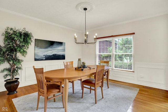 5761 Coopers Hawk Dr, Carmel, IN 46033 - dining space with a chandelier, light wood-style flooring, crown molding, wainscoting, and a decorative wall