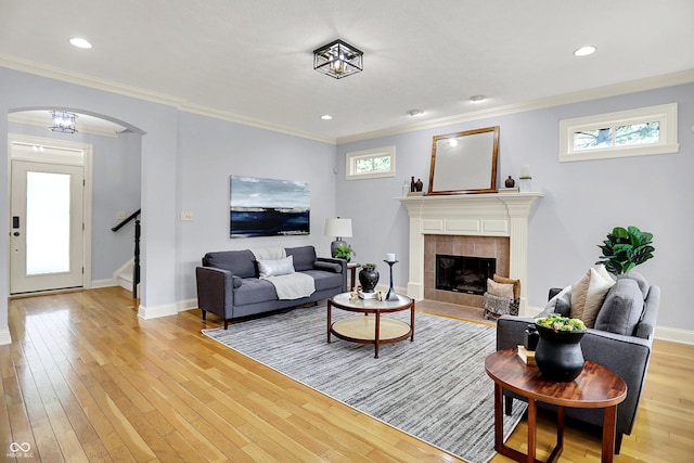 2263 Glebe St, Carmel, IN 46032 - living room with arched walkways, ornamental molding, light wood-style flooring, a tiled fireplace, and stairs