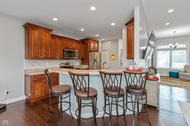 1976 Austin James Ln, Seymour, IN 47274 - kitchen with appliances with stainless steel finishes, dark wood-style flooring, decorative backsplash, a kitchen breakfast bar, and light countertops