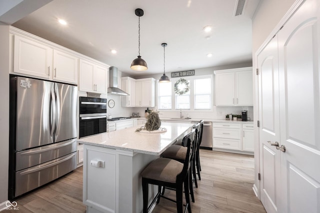 2856 Old Rosebud Ln, Westfield, IN 46074 - kitchen featuring appliances with stainless steel finishes, wall chimney exhaust hood, a breakfast bar area, a kitchen island, and white cabinetry