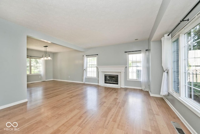8909 Carnation Dr, Noblesville, IN 46060 - unfurnished living room with a chandelier, light wood finished floors, a glass covered fireplace, and a textured ceiling