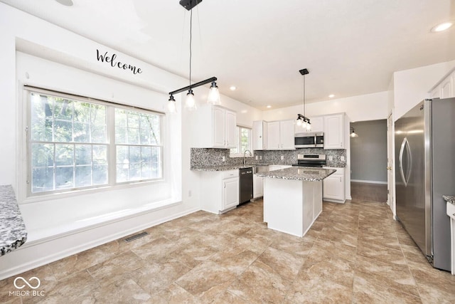 8909 Carnation Dr, Noblesville, IN 46060 - kitchen featuring appliances with stainless steel finishes, a center island, decorative backsplash, white cabinetry, and light stone counters