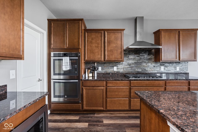 6176 Brighton Dr, Whitestown, IN 46075 - kitchen with wall chimney exhaust hood, stainless steel appliances, dark wood finished floors, dark stone countertops, and decorative backsplash