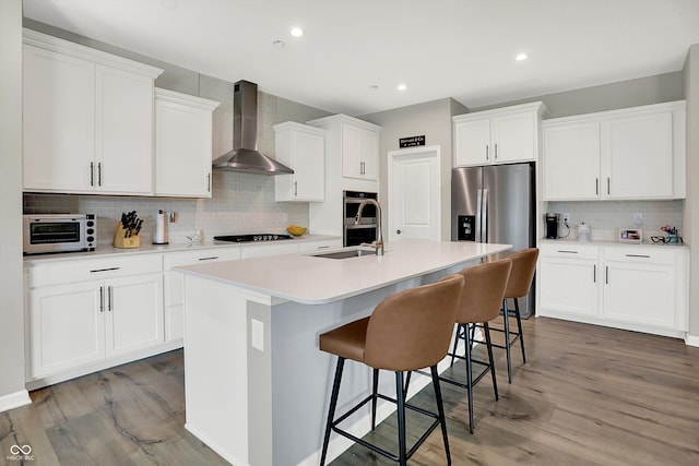 1319 Petit Verdot Dr, Westfield, IN 46074 - kitchen featuring wall chimney exhaust hood, appliances with stainless steel finishes, decorative backsplash, a center island with sink, and wood finished floors
