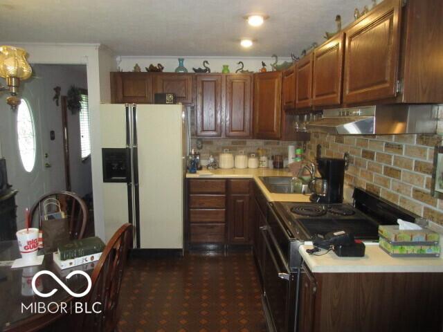2610 Marywood Dr, Southport, IN 46227 - kitchen featuring stove, white fridge with ice dispenser, light countertops, range hood, and tasteful backsplash