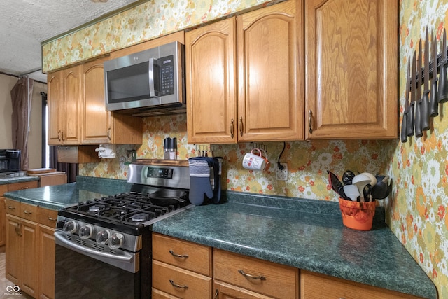 3534 Carr Ave, Indianapolis, IN 46221 - kitchen featuring stainless steel appliances, wallpapered walls, a textured ceiling, dark countertops, and brown cabinets