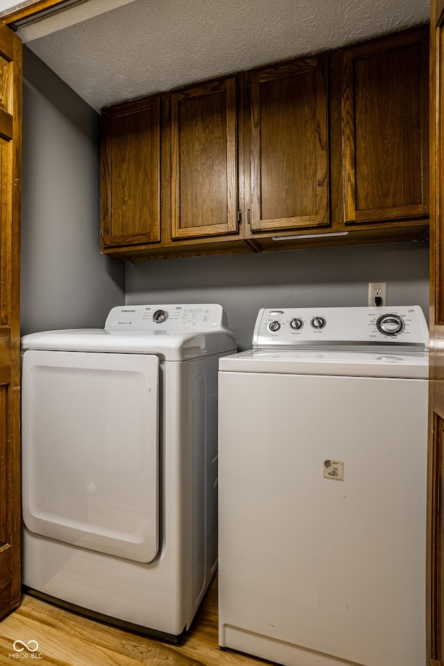 2411 N Willow Way, Indianapolis, IN 46268 - laundry room featuring washer and dryer, light wood-style flooring, cabinet space, and a textured ceiling