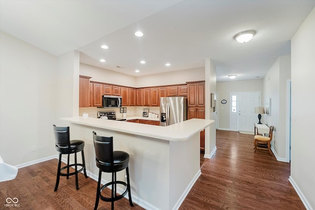 5651 Jones Dr, Plainfield, IN 46168 - kitchen featuring appliances with stainless steel finishes, a kitchen bar, dark wood-type flooring, a peninsula, and light countertops